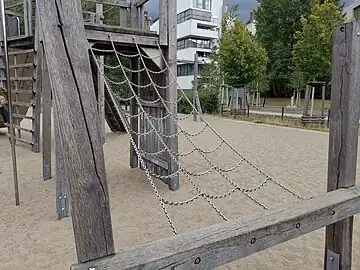 Ein Klettergerüst aus Ketten, das zu einer Platform führt, die Teil einer komplexen Anlage ist. climbingframe + material=chain, platform, structure