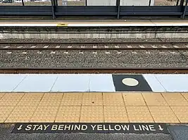 A row of bright yellow blister tactile paving in front of a rail platform
