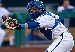 Austin Nola in royal blue catching gear and a white Omaha Storm Chasers uniform, holding his catchers mitt out to his left