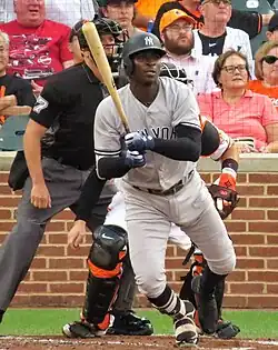 Didi Gregorius in a gray New York Yankees jersey in 2018, exiting the batter's box in front of a catcher and umpire