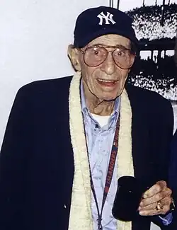 Eddie Layton wearing a New York Yankees cap and holding a mug