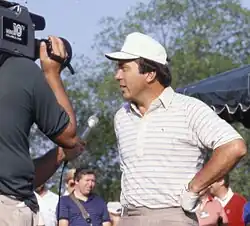 Johnny Bench at a 1984 golf tournament, wearing a white hat and being interviewed in front of a TV camera