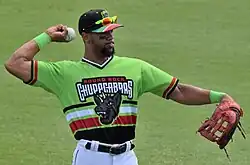 Leody Taveras throwing a baseball in a grassy outfield, wearing a green Round Rock El Chupacabras uniform