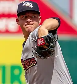 A baseball player in a white uniform, mid-pitch.