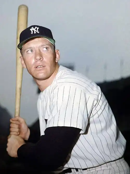 Medium-wide shot of baseball player Mickey Mantle, swinging a bat and wearing a "NY" shirt and hat.