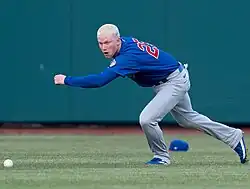 Pete Crow-Amstrong, with blond hair and his hat in the background, running toward a baseball on the ground in the outfield of an Iowa Cubs game in 2024