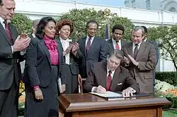 Ronald Reagan at the signing ceremony for Martin Luther King Jr. Day legislation in the Rose Garden. Coretta Scott King, George H. W. Bush, Howard Baker, Bob Dole, Jack Kemp, Samuel Pierce, and Katie Hall looking on.