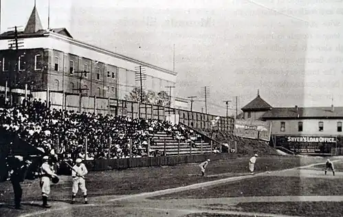 A black and white photograph of home plate and the left field bleachers at a ballpark.