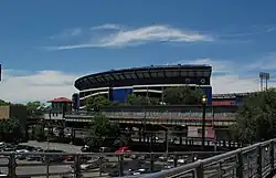 View from the Mets-Willets Point station's platform, with the former Shea Stadium in the background. A black fence, which surrounds the platform, is visible on the bottom right corner.