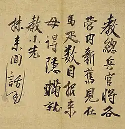 A close-up view of Chinese calligraphy written in bold black ink on aged, tan paper. The script is arranged in vertical columns, likely in the semi-cursive style, with an appended note of smaller characters on the left edge.