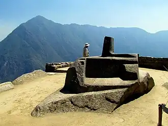 Intihuatana stone with the mountain ridge visible behind.