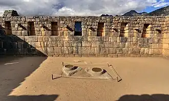 Stone wall with trapezoidal niches, with two carved circular stone basins on the ground in front.