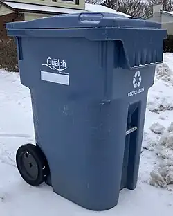 A blue recycling bin with wheels used for residential collection. There is snow in the background.