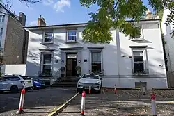 A two-storey white building with grey window frames, several cars parked in the foreground
