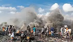 Several people are working on a heap of rubbish, with smoke rising from it.