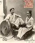Two women wear áo ngũ thân, the predecessor of the áo dài initially worn in the 18th century.