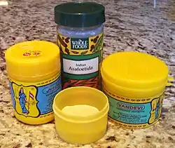 Color photograph of four plastic containers; in the foreground, the open container holds a yellow powder.