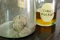 Two glass containers, one holding pieces of resin with plant debris, the other an orange-yellow tincture.