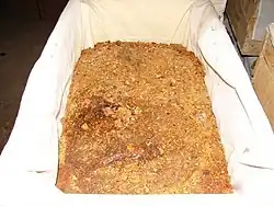 Close-up of a wooden crate lined with white fabric and filled with resin pieces of varying sizes, light yellow to dark brown in color.