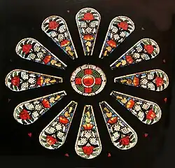 a small round stained glass window surrounded by twelve panels featuring floral designs of large red and small white flowers