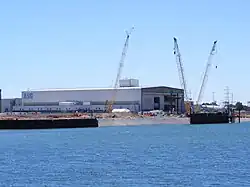 A long, wide building on the shore of a river, with the letters "ASC" on the visible faces.