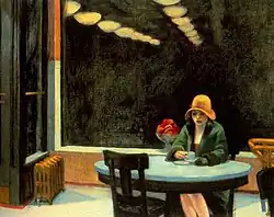 A woman sits alone at a table with a coffee cup in a brightly lit automat