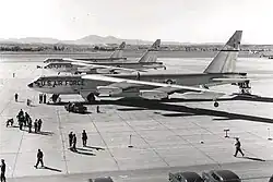 Black-and-white photo of three B-52s parked close together facing left, as personnel on the ground prepare them for departure