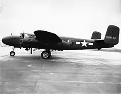Black-and-white photo of an early bomber parked perpendicular to the camera, facing left, rearward of the wing is a star in front of horizontal stripes