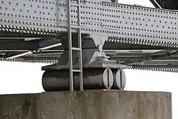 Two cylinders of steel, supporting a large steel bridge, and resting on a concrete support
