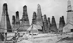 A black-and-white photograph showing a field of derricks each completely enclosed within its own oddly shaped wooden building.