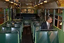 Barack Obama sitting on the Rosa Parks bus, looking thoughtfully out through the window