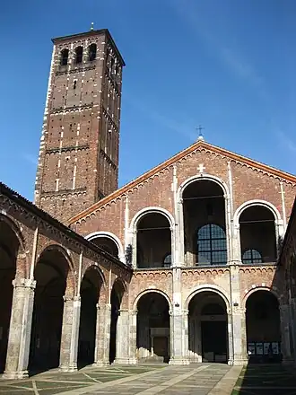 The façade and forecourt of a redbrick church are composed of simple arcades. A brick tower rises up to one side.