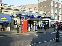 A white-bricked building with a clear, sloped roof and a sign that reads "BAYSWATER STATION" in white letters on a blue background