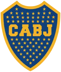 A Blue shield with a golden border. Inside the shield, 67 stars inside the shield with the golden letters "CABJ" (meaning "Club Atlético Boca Juniors") printed around the center, separating the stars