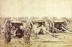 An old photograph showing a group of field artillery pieces and caissons with a line of soldiers in the background