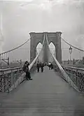 A black-and-white view of the Brooklyn Bridge in 1899 looking east on the pedestrian walkway