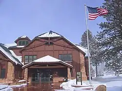 Two story wood building next to flag pole with U.S. flag waving in the wind. Snow on the ground.
