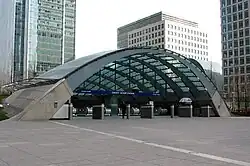 A wide, grey archway with a blue sign reading "CANARY WHARF STATION" in white letters and a man in a black suit walking through