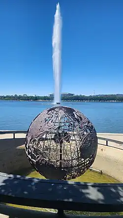 A large metal wire globe depicting the travels of Captain Cook stands on a concrete platform on the shore of the lake, amidst landscaped parks.
