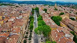 Aerial view of Cours Mirabeau, a tree-lined avenue in Aix-en-Provence, showing dense historic rooftops and the surrounding Provençal landscape