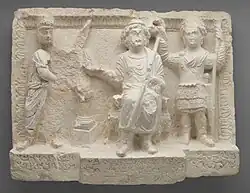 Limestone relief sculpture with three figures, the one on the right (in military dress) holding a crown over the head of the figure in the middle.
