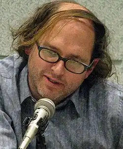 Daniel Waters, seated at a table and speaking into a microphone