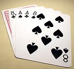 A 5-card stud poker hand lays on a table showing black aces and eights, with the hole-card face down