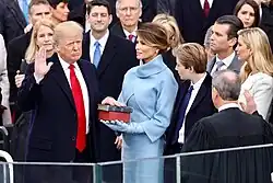 Trump, with his family watching, raises his right hand and places his left hand on the Bible as he takes the oath of office. Roberts stands opposite him administering the oath