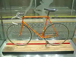 An orange bicycle behind glass.