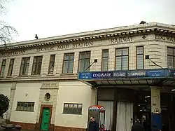 A tan-coloured building with brown-framed windows and a sign reading "METROPOLITAN EDGWARE ROAD STATION RAILWAY" in brown letters