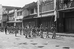 A section of Indonesian soldiers marches through an empty street. 12 November 1949