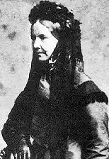 A woman, seen in three-quarter profile, in black, wearing a black headdress.