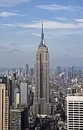 Aerial view of a 100-story building with several setbacks; the building tapers into a large circular spire near its 90th floor and is topped by a large antenna.