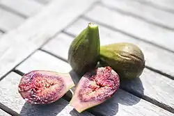 Whole figs and sliced fig halves arranged on a wooden tabletop in natural light